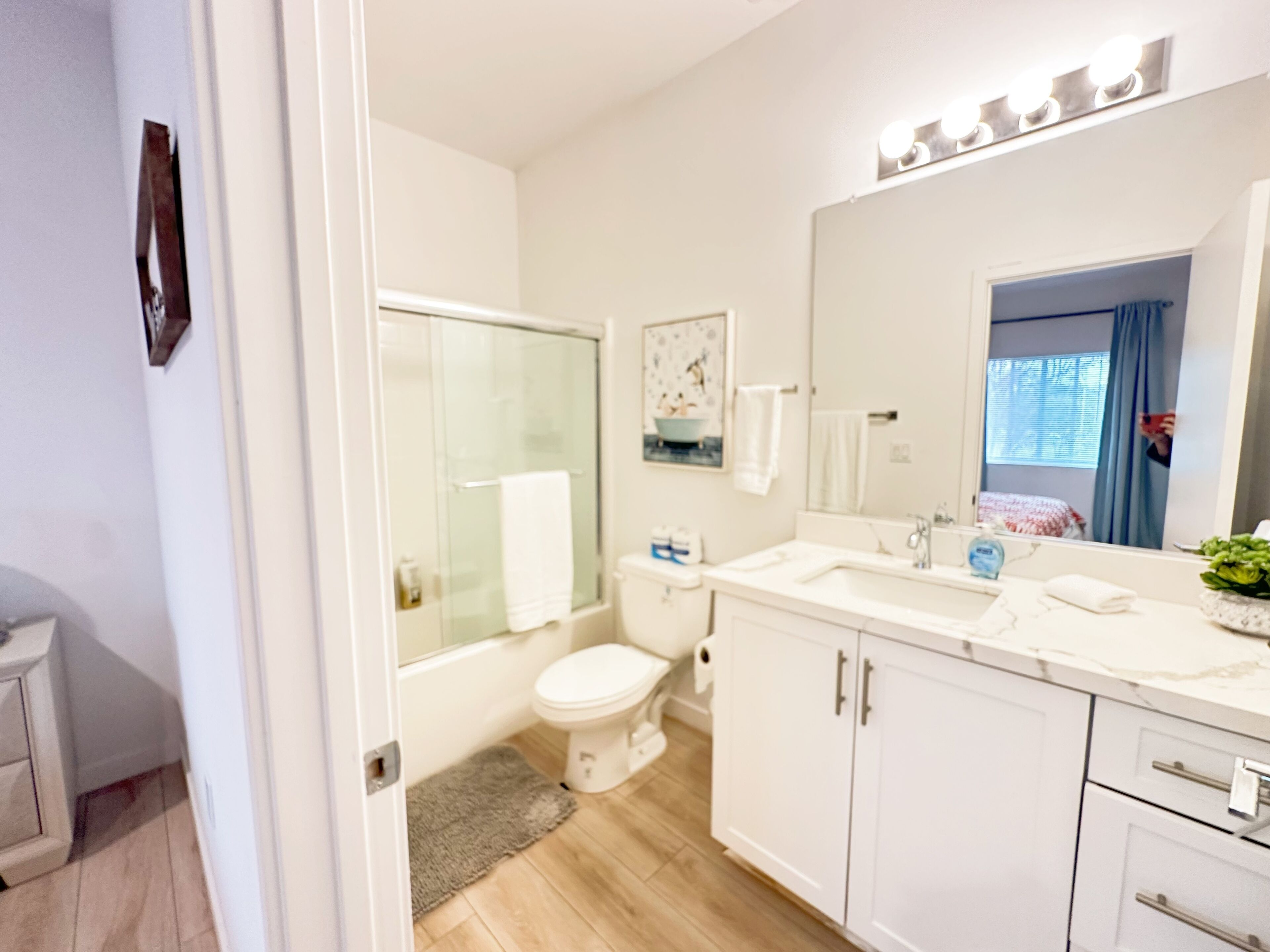 Een moderne badkamer met een glazen douchecabine, toilet, wastafel met spiegel en een badkamermeubel met kastjes.