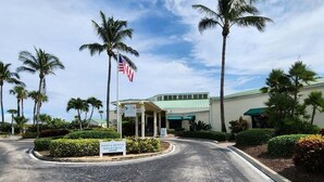 A building with a sign for a sales and rental department, surrounded by palm trees and a clear sky.