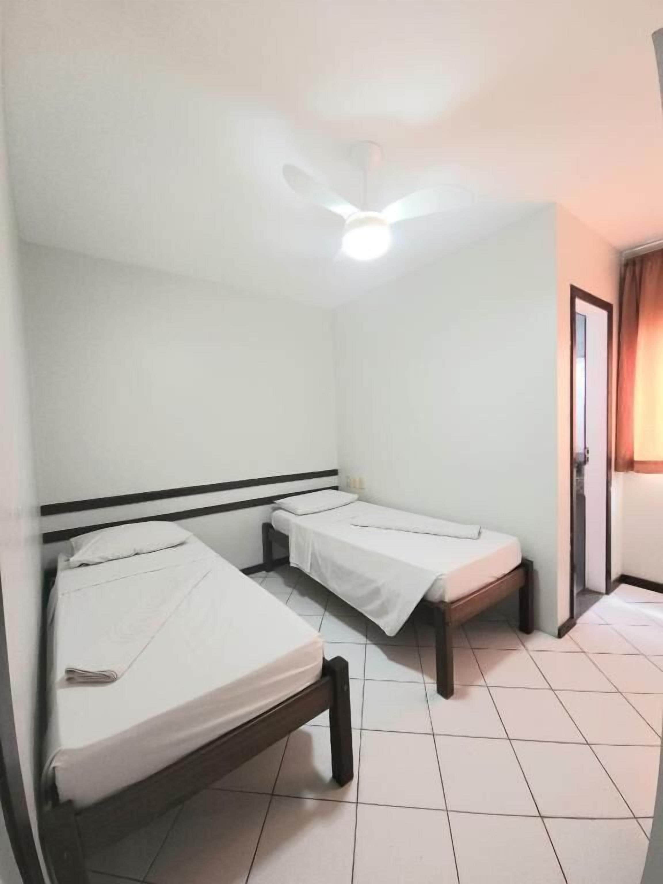 Una habitación con dos camas individuales, un ventilador de techo y una puerta que da a otra habitación.