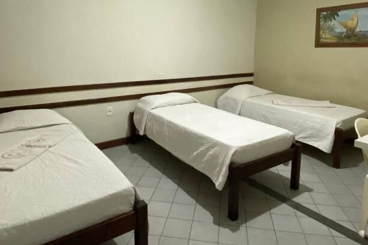 A room with three single beds, a white chair, and a painting on the wall.