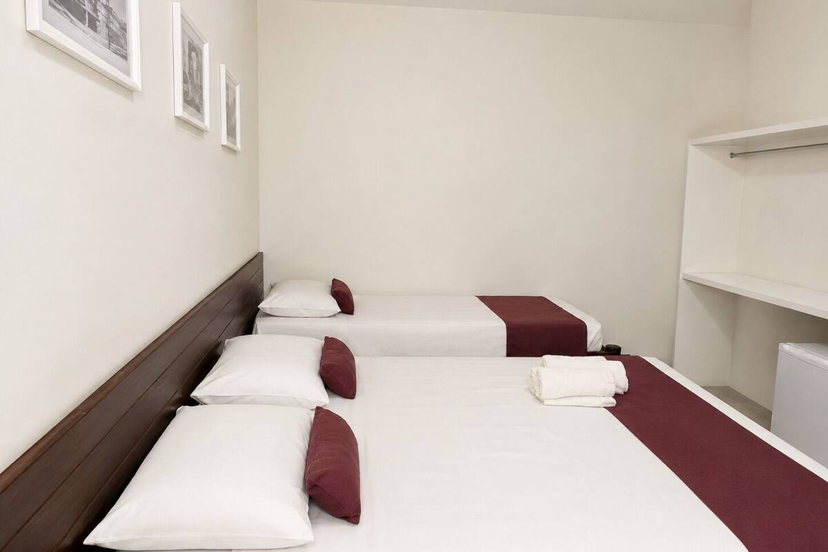 A hotel room with three beds, white bedding, and a red accent.