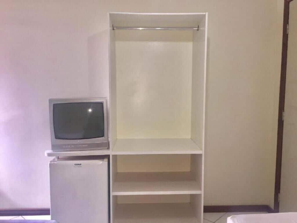 A room with a white wardrobe, a small refrigerator, and a television on top of the fridge.
