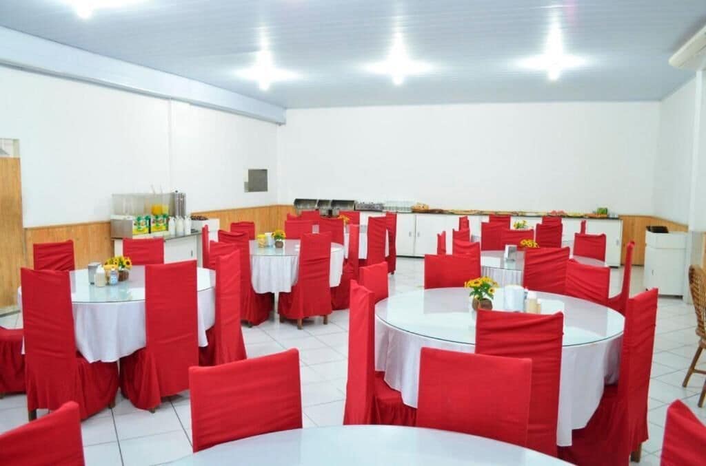 A dining area with round tables covered with white tablecloths and red chairs.