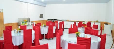 A dining area with round tables covered with white tablecloths and red chairs.