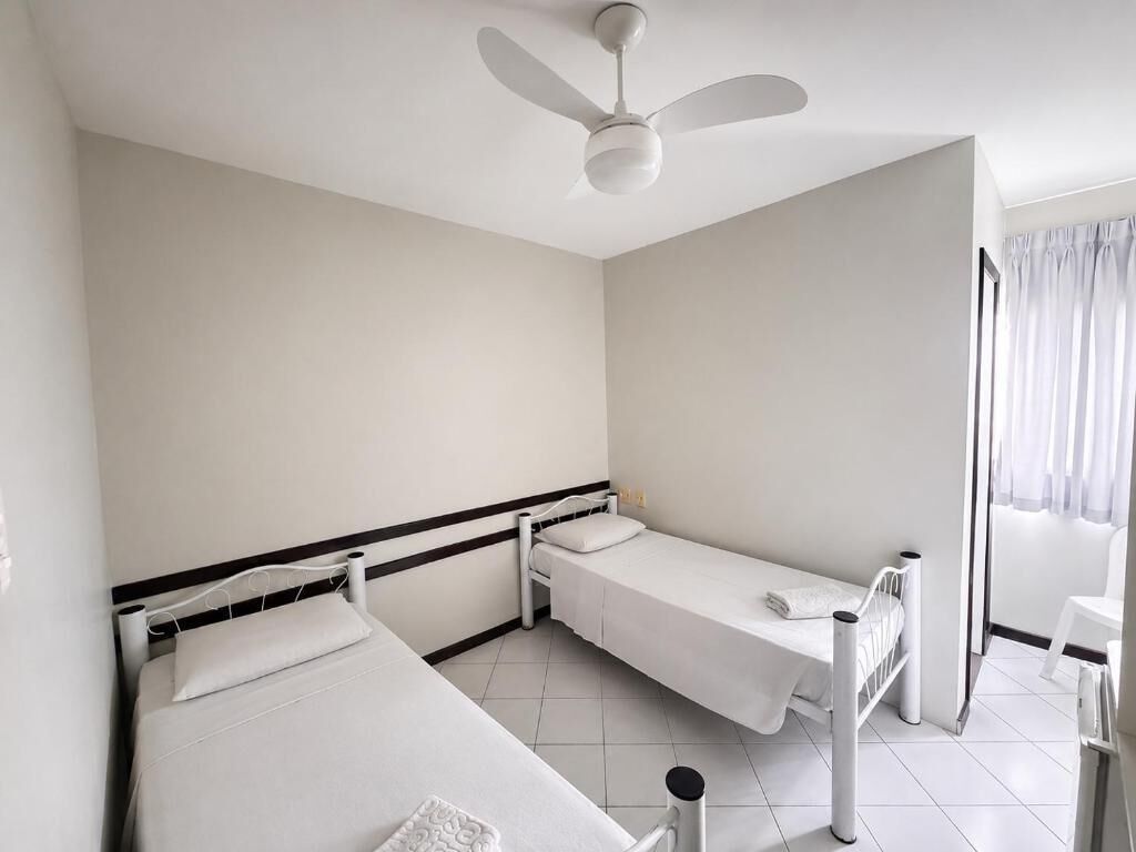 Una habitación con dos camas individuales, un ventilador de techo, una ventana con cortinas y una mesita pequeña.
