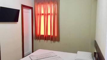 A hotel room with a bed, a flat-screen TV mounted on the wall, and a window with curtains.