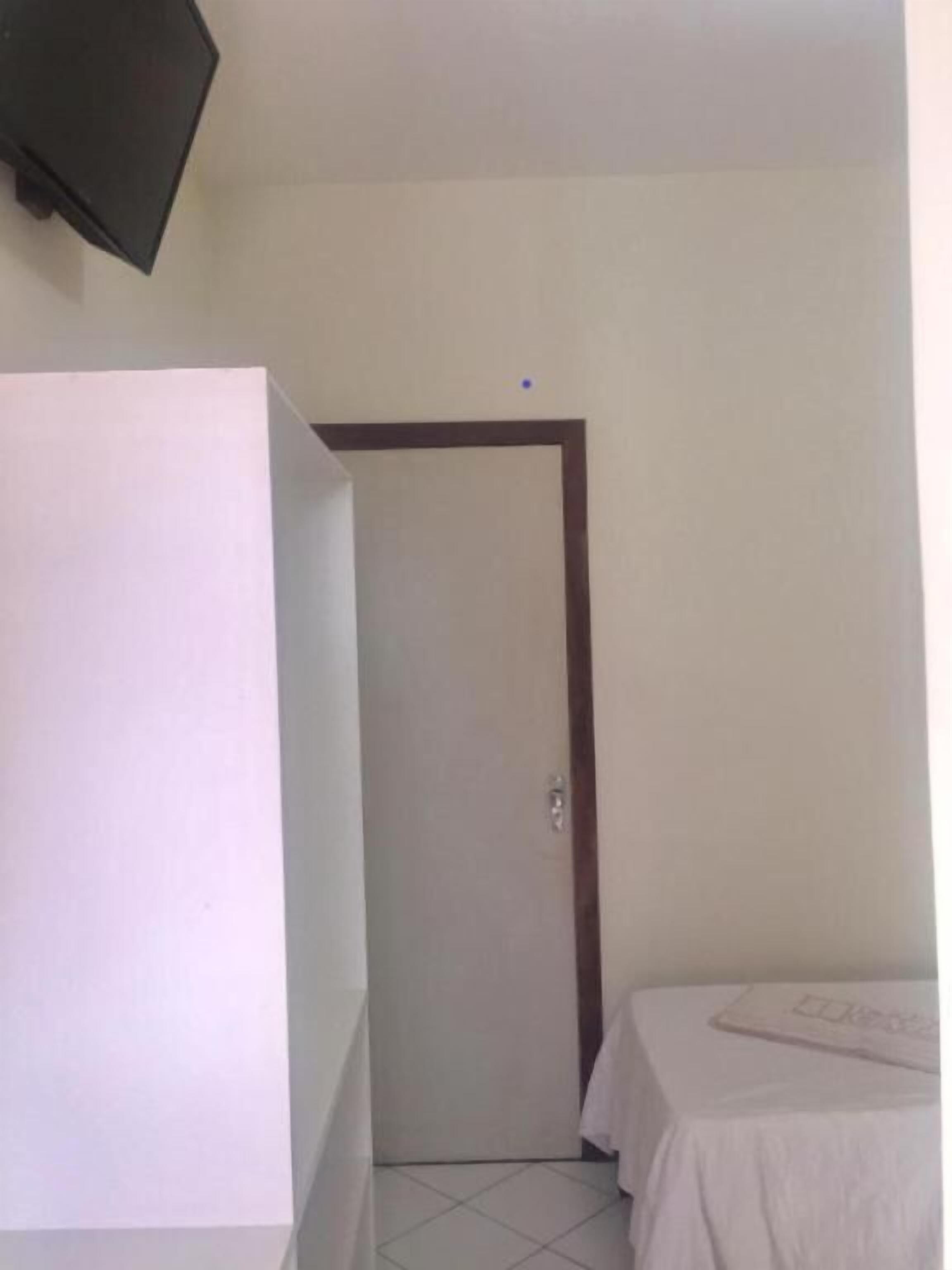 A small, clean room with a bed, a door, and a television mounted on the wall.