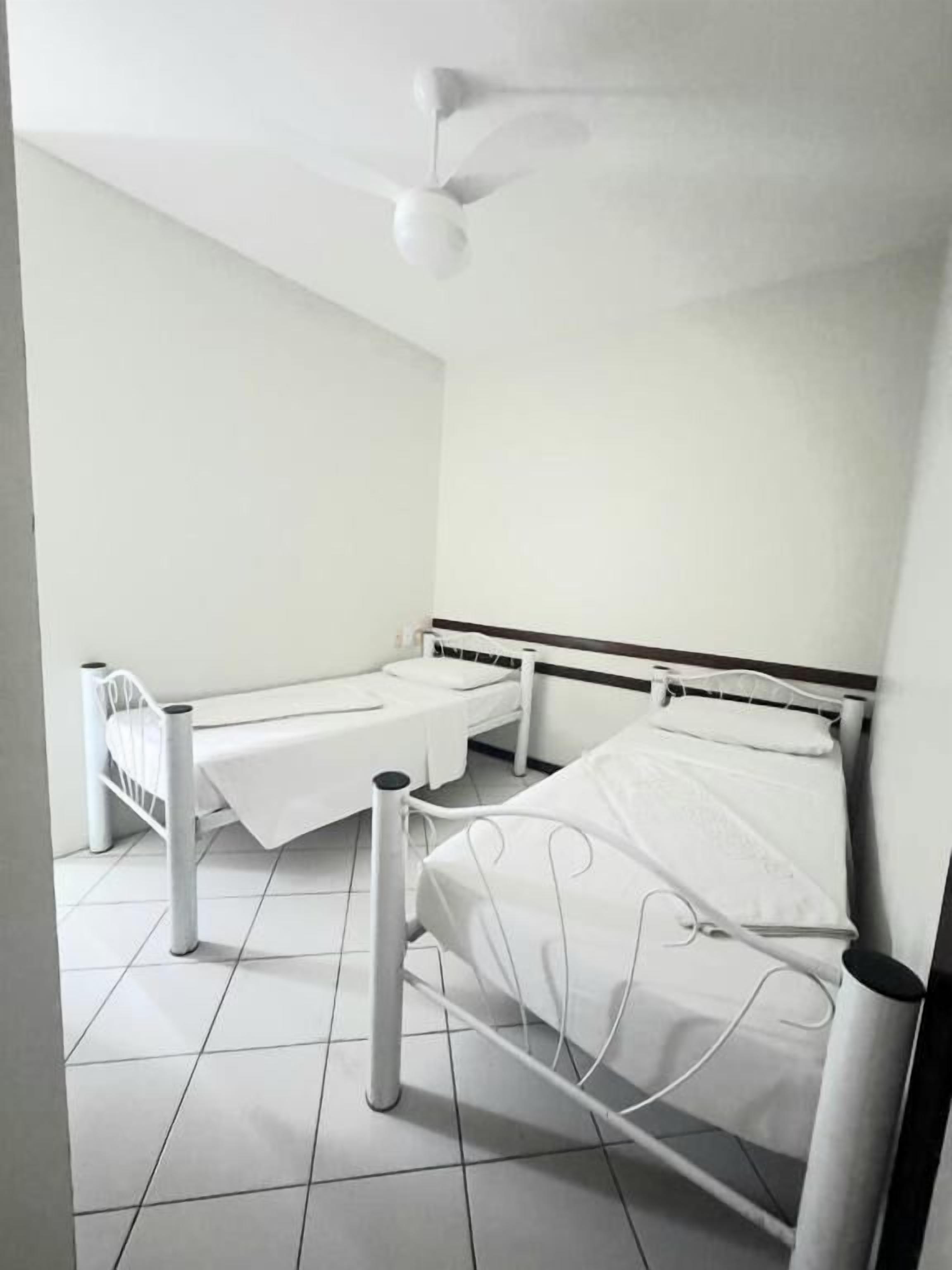 A room with two beds, a ceiling fan, and a white tiled floor.