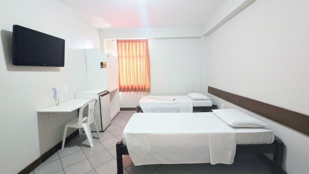 Una habitación de hotel con cama, escritorio, silla, televisor y ventana con cortinas.