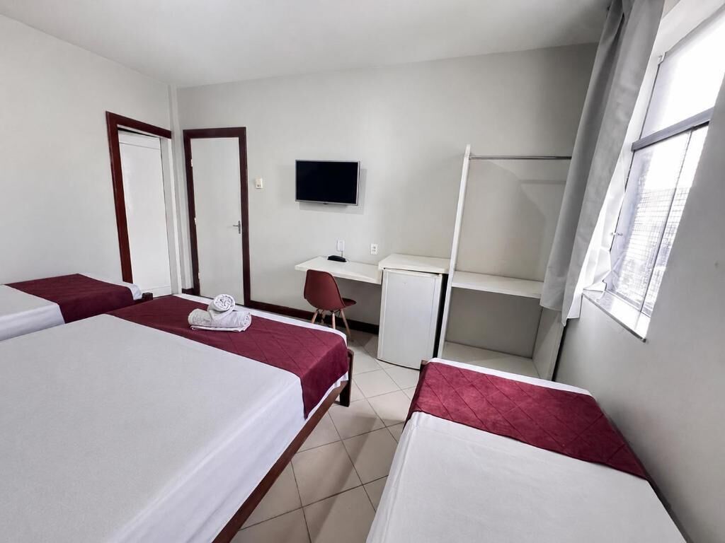 A hotel room with two beds, a desk, a chair, a TV, and a shower.