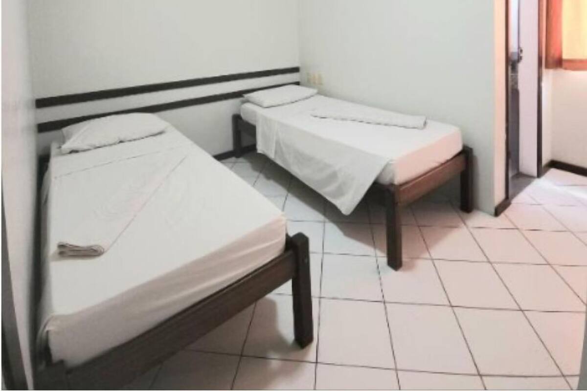A small, clean room with two single beds, a ceiling fan, and a door leading to another room.