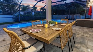 An outdoor dining area with a pool, wicker chairs, and a wooden table set for a meal.