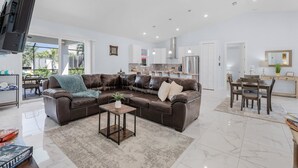 A modern living room with a brown leather sofa, a small coffee table, and a dining area with a table and chairs.