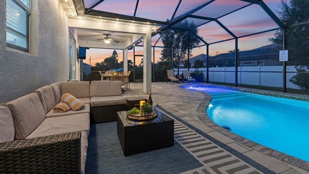 A covered outdoor area with a pool, seating, and a view of the sunset.