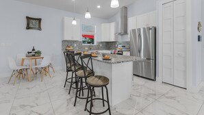 A modern kitchen with white cabinets, a stainless steel refrigerator, and a marble countertop.