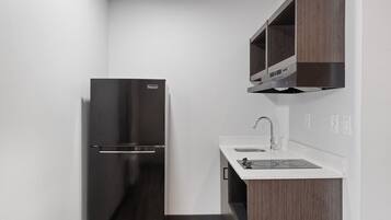 Una cocina compacta con un refrigerador negro, un mueble de madera sobre el fregadero y una encimera blanca.