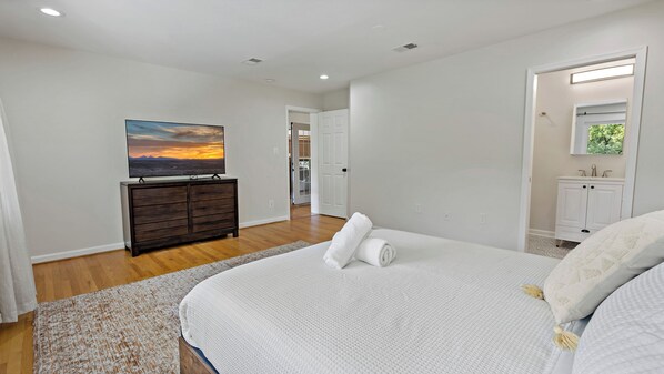 A bedroom with a bed, a dresser, a painting, and a bathroom visible through an open door. - Stay,Work,Thrive on the premier House, Entire home in McLean (McLean)