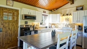 Cucina con soffitto in legno, mobili bianchi, un tavolo da pranzo in legno e un piano cottura.