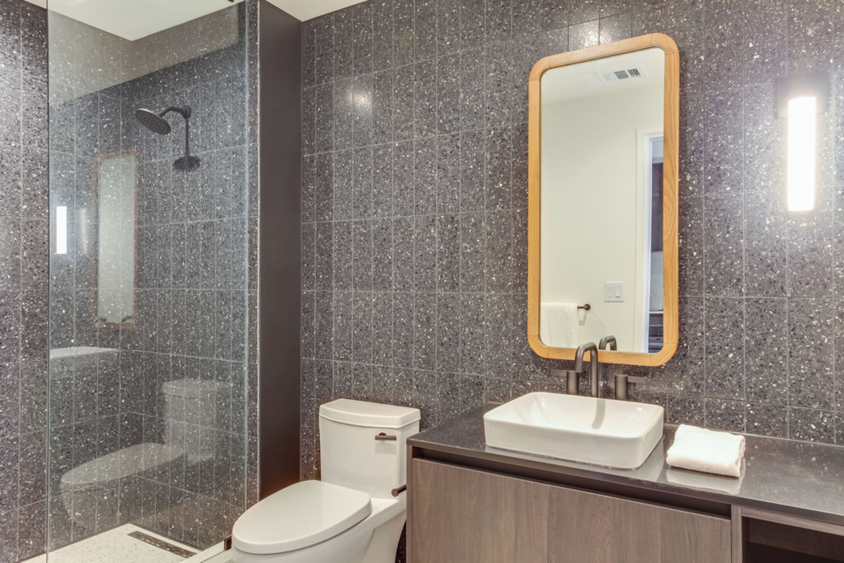 A modern bathroom with a glass-enclosed shower, a white toilet, and a wooden vanity with a sink and mirror.