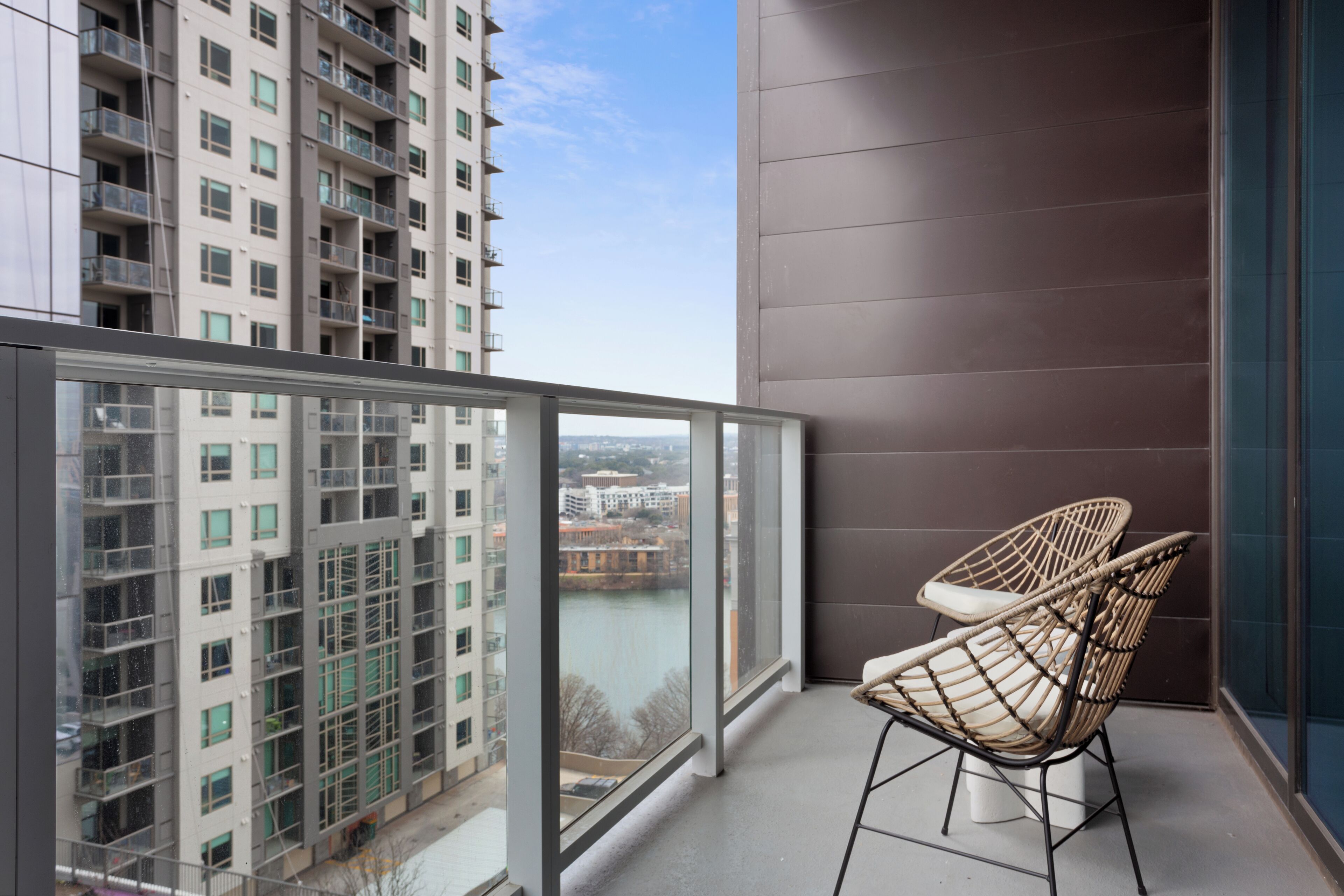 A balcony with a view of a river and high-rise buildings. There are two wicker chairs.