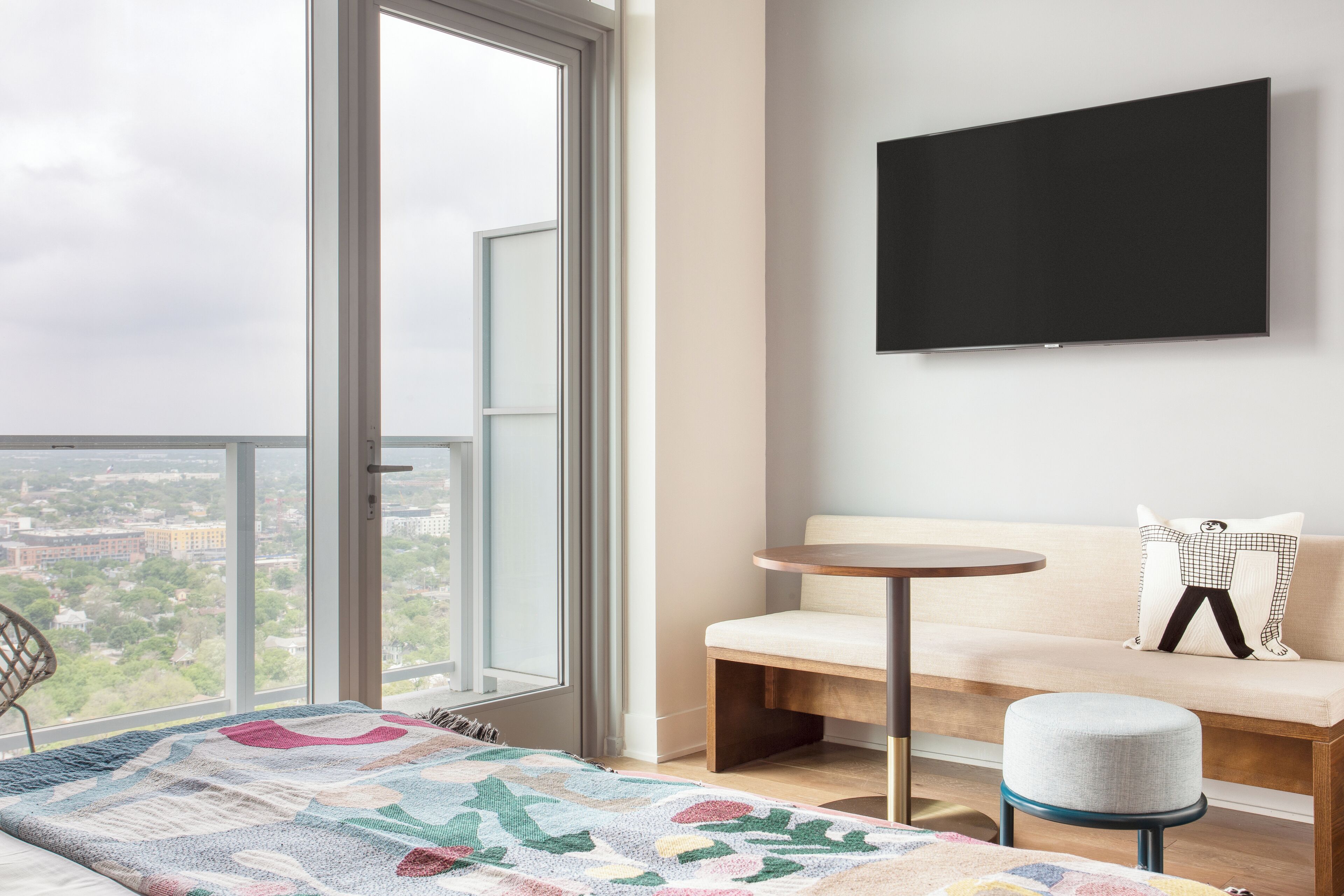 Ein modernes Hotelzimmer mit großem Fenster, einer Couch, einem kleinen runden Tisch und einem wandmontierten Flachbildfernseher.