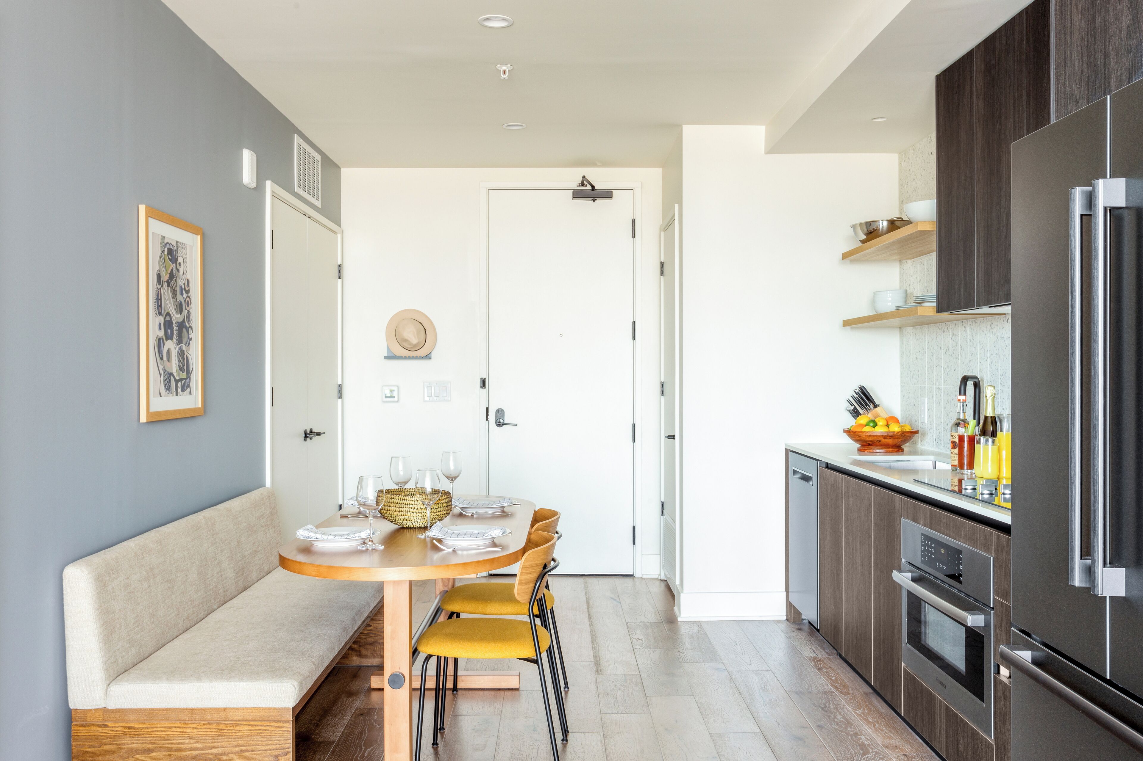 A modern kitchen with a built-in oven, a refrigerator, and a dining area with a bench and chairs.