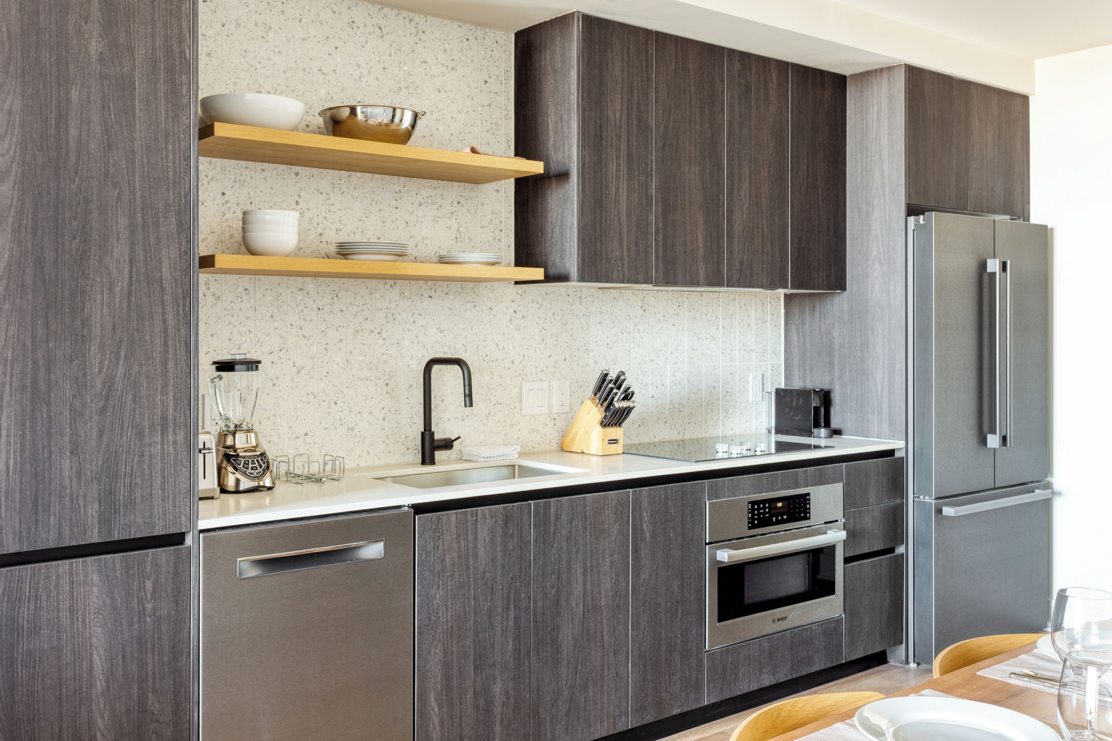 A modern kitchen with dark wood cabinets, stainless steel appliances, and wooden shelves.