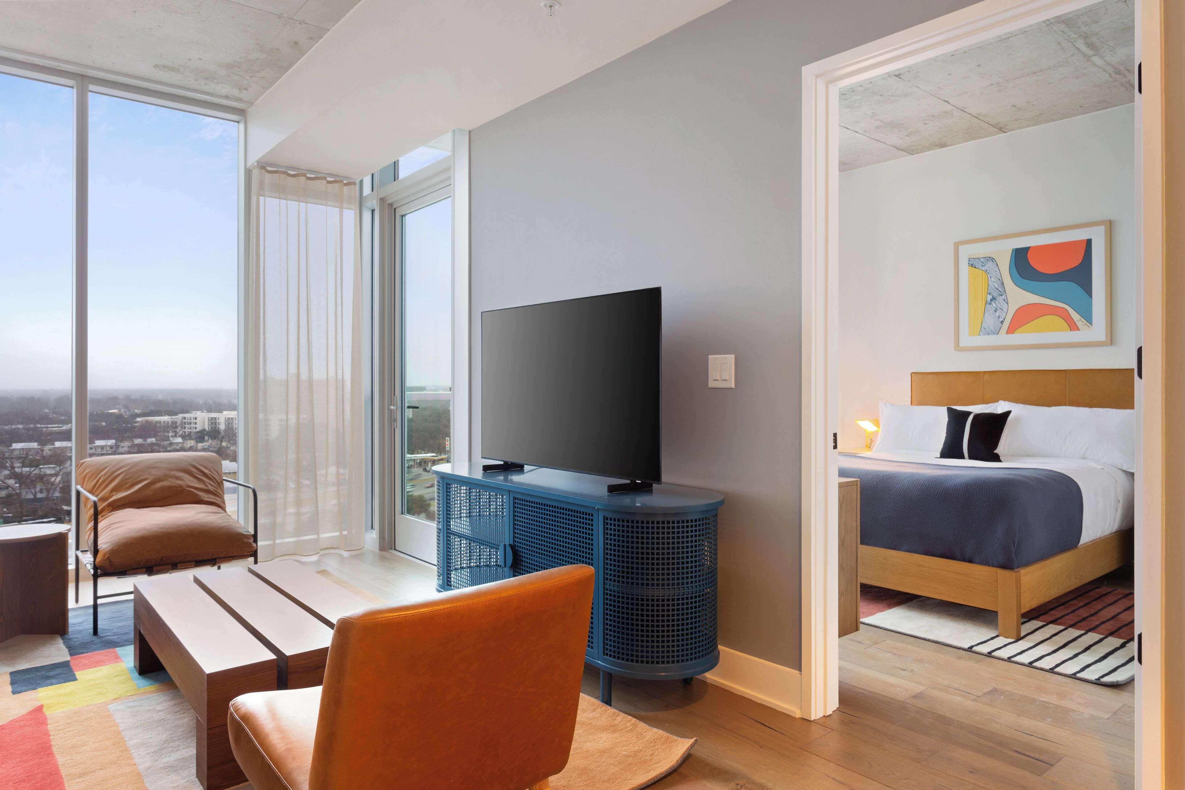 Ein modernes Hotelzimmer mit großem Fenster, Flachbildfernseher, Bett und einer kleinen Sitzecke.