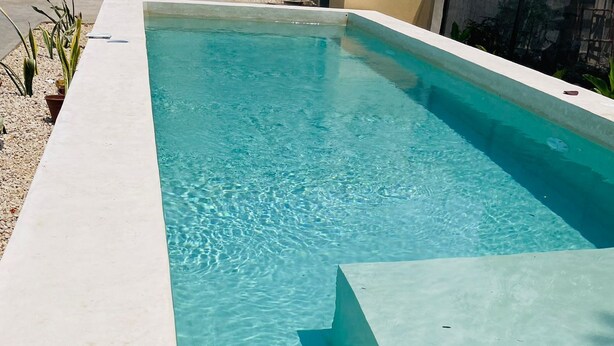 A rectangular swimming pool with clear blue water, surrounded by a light-colored deck.