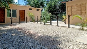 A courtyard with a gravel path, a wooden deck, and a building with a beige exterior and wooden doors.
