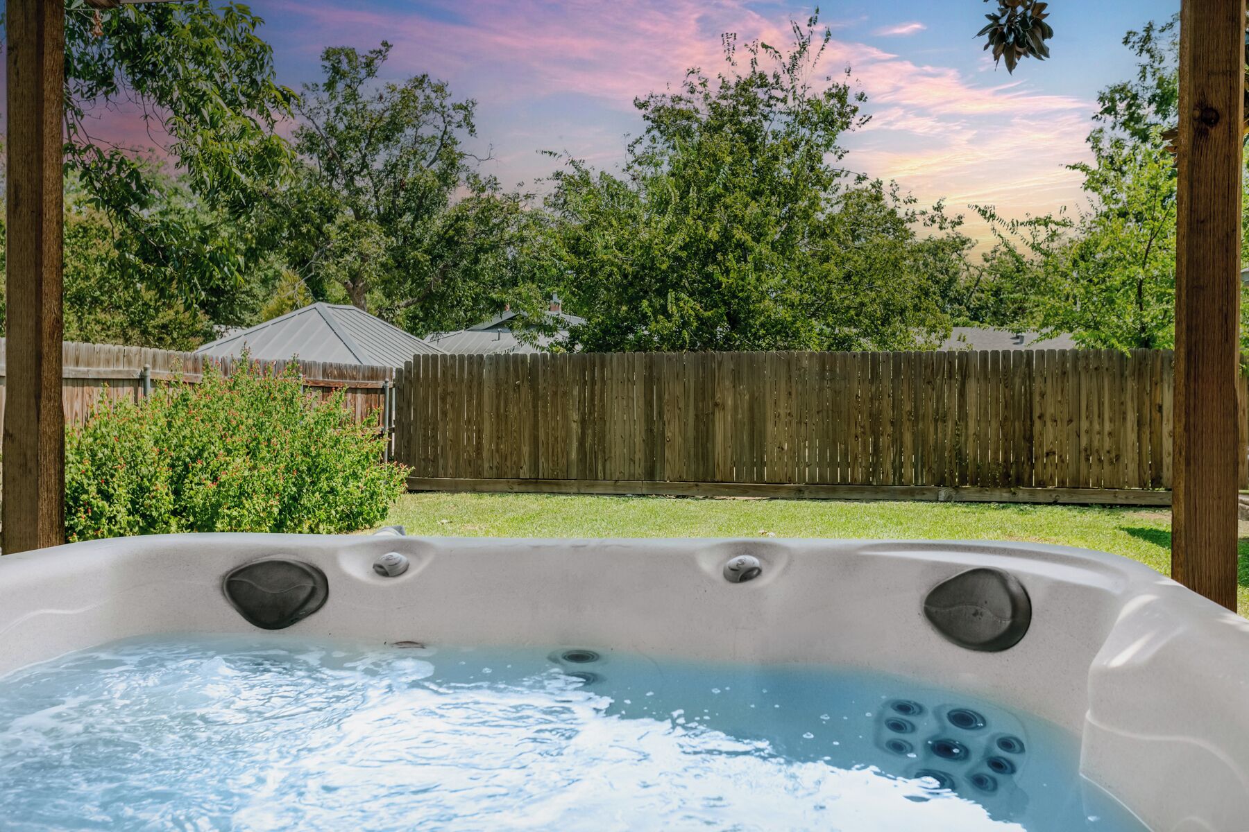 Un jacuzzi en un patio trasero con una valla de madera y árboles al fondo.
