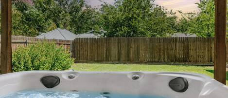 Un jacuzzi en un patio trasero con una valla de madera y árboles al fondo.