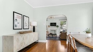 A dining area with a wooden table, chairs, a white cabinet with geometric patterns, and framed artwork on the wall. - Magnolia Cottage | 3/2, Full Kitchen, Hot Tub, Grill, 3 Blocks to Main (Fredericksburg)