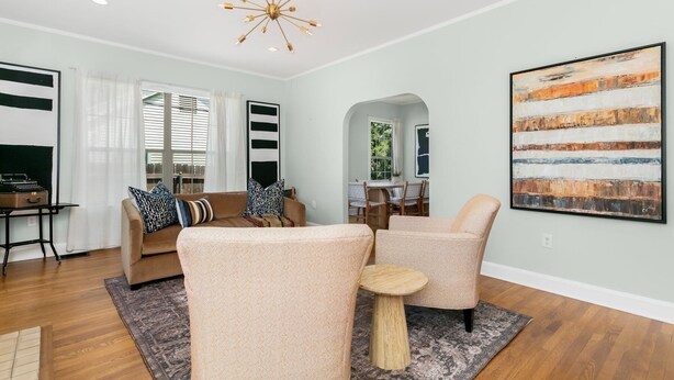 A modern living room with a beige sofa, two armchairs, a coffee table, and a large abstract painting on the wall. - Magnolia Cottage | 3/2, Full Kitchen, Hot Tub, Grill, 3 Blocks to Main (Fredericksburg)