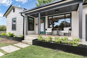 Une maison moderne dotée d’un porche abrité, de deux chaises blanches et d’une table.