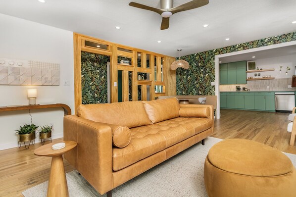 Un salon moderne avec un canapé en cuir, un pouf rond et une table basse en bois.