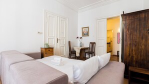 Ein Zimmer mit einem Bett, einem Holzschrank, einem Esstisch mit Stühlen und einer durch eine offene Tür einsehbaren Küche.