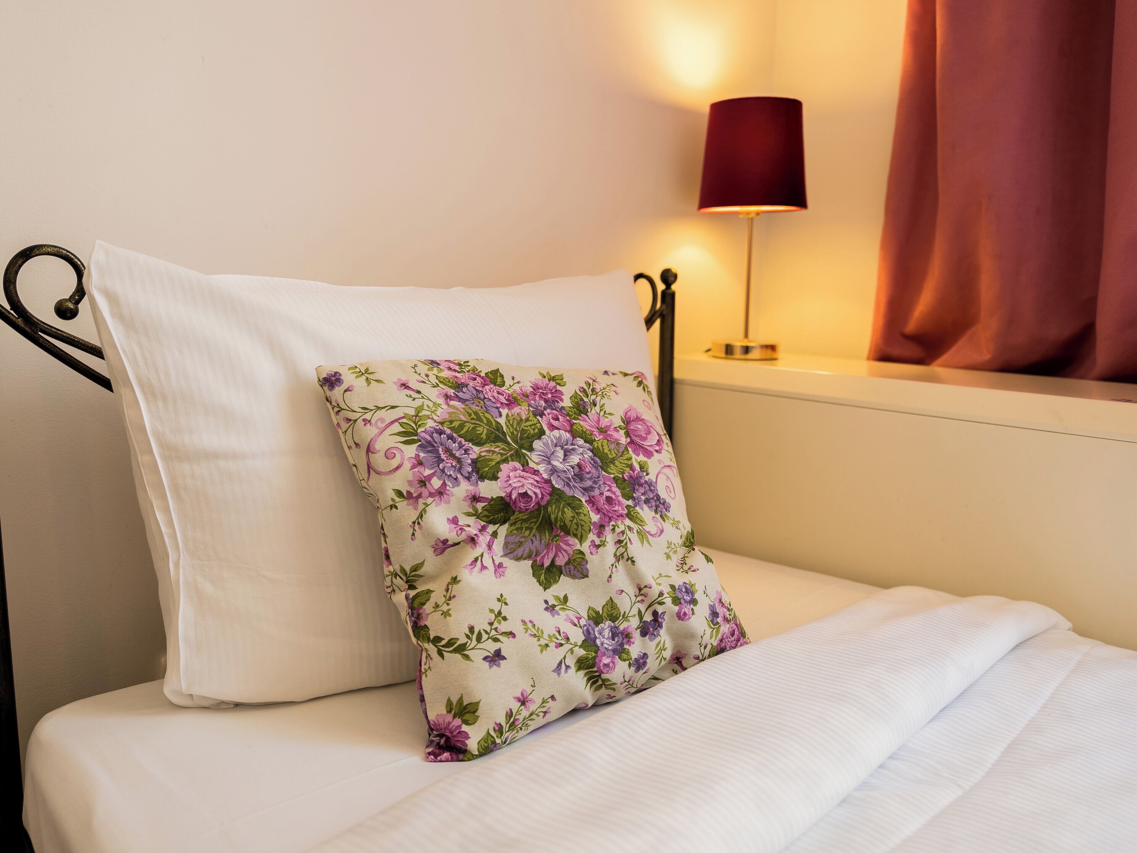 A neatly made bed with a white pillow and a floral pillow.