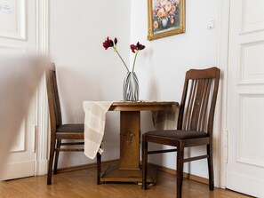 Ett hörnrum med ett träbord, två stolar, en vas med blommor och en inramad tavla på väggen.