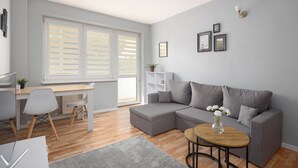 Una sala de estar moderna con un sofá gris, una mesa de centro de madera y una zona de comedor con una mesa y sillas blancas.