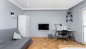 A modern room with a grey sofa, a TV mounted on the wall, a desk with a chair, and a bed.