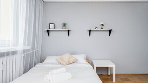 A neatly arranged bedroom with a bed, two bedside tables, and two wall-mounted shelves with decorative items.