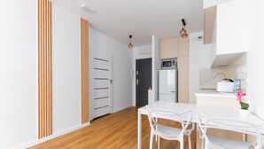 A modern kitchen with white cabinets, a microwave, and a toaster. There is a dining table with white chairs. - Park Skowroni Cosy Apartment (Wrocław)