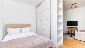 A modern bedroom with a bed, a wardrobe, a TV, and a seating area. - Park Skowroni Cosy Apartment (Wrocław)