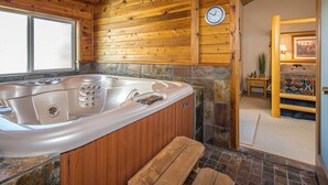 L’intérieur d’un chalet en bois, avec un bain à remous, des murs en pierre, un banc en bois et une horloge au mur.