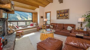 Un salon chaleureux avec une cheminée, des canapés en cuir, une table basse en verre et une vue sur les montagnes.