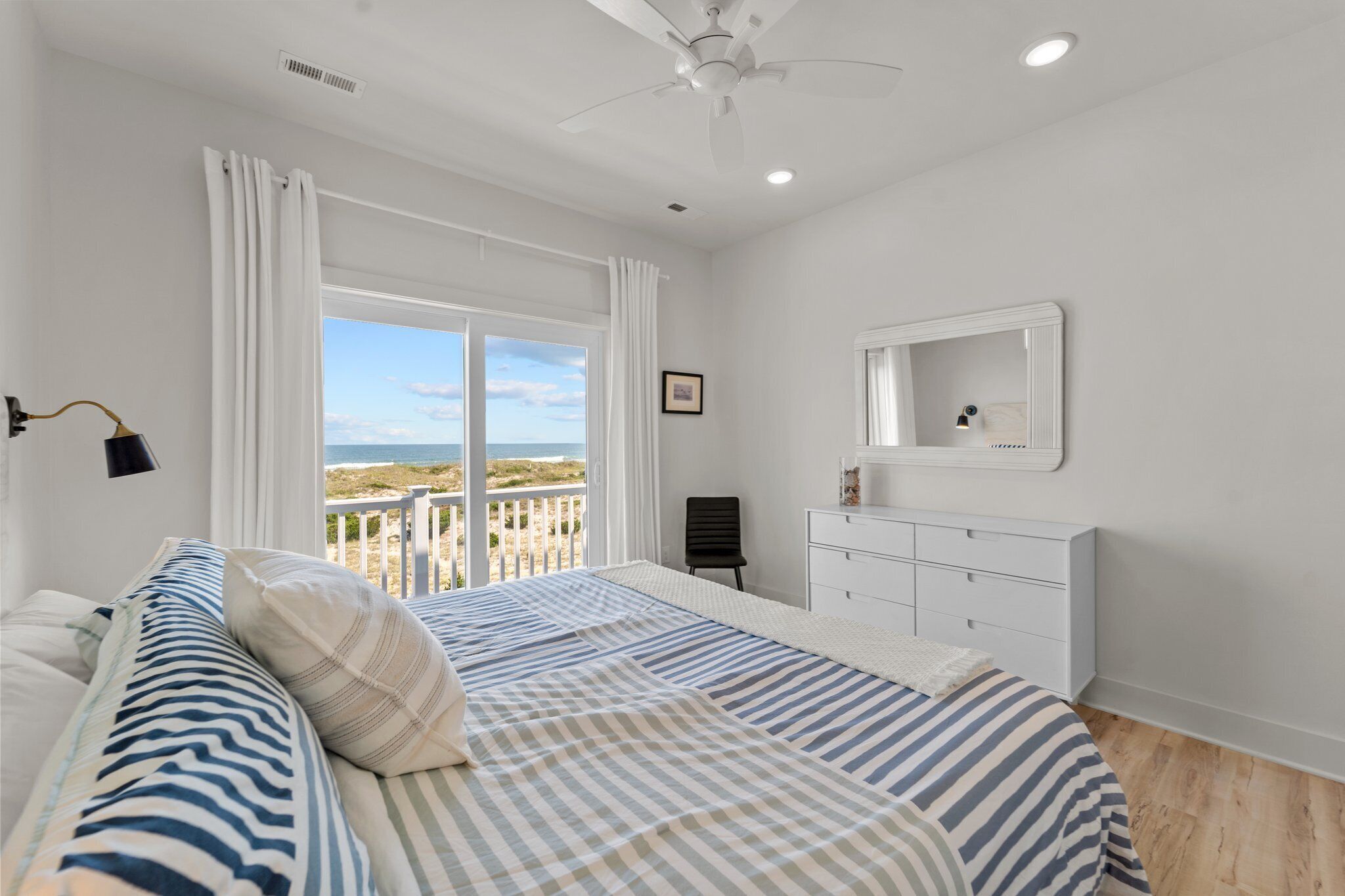 A bedroom with a large bed, a dresser, a chair, and a view of the beach.