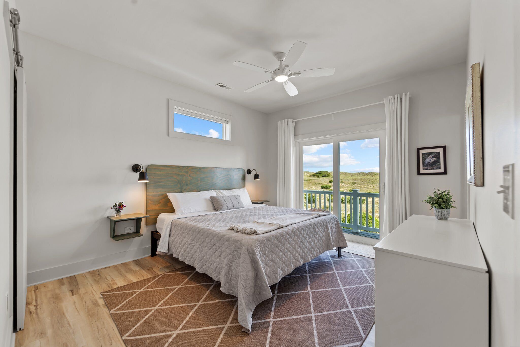 A bedroom with a bed, a nightstand, a ceiling fan, a window, and a view of the outdoors.