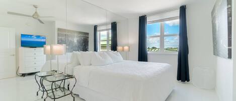 A modern bedroom with a large bed, a ceiling fan, a TV, and a view of the outdoors.