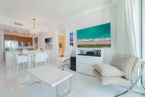 Uma sala de estar moderna com uma mesa de jantar branca, um sofá bege e uma pintura grande de uma praia.